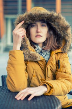 Sarışın, beyaz bir kadın kışı dışarıda geçirir. Güzel kız, şehir portresi. Moda modeli oturuyor ve kameraya bakıyor.