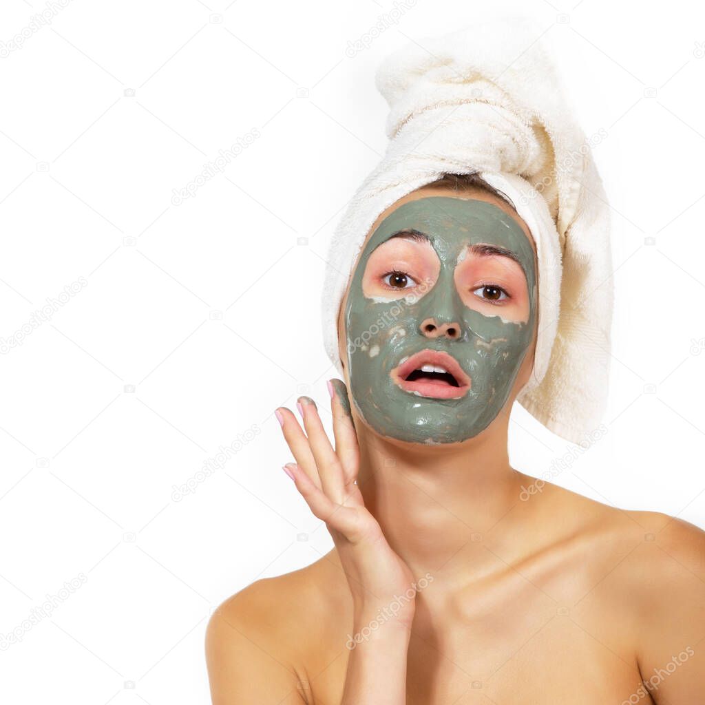 Beautiful cheerful girl applying facial clay mask. Young woman and beauty treatments over white background. Pampering, youth, anti-aging, body care spa theme. Female face with cosmetics mask