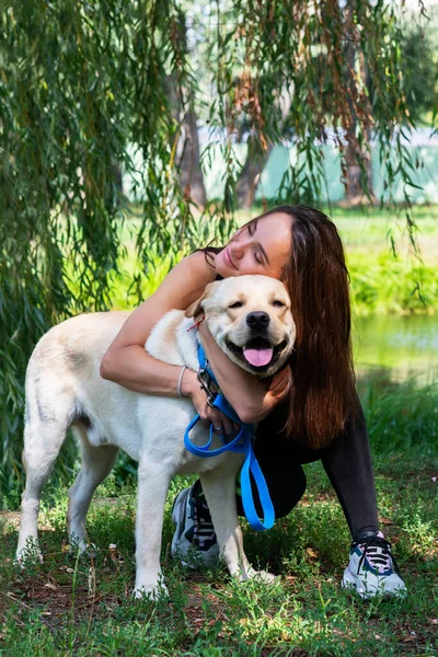 Fröhliche Hübsche Junge Frau Sitzt Und Umarmt Ihren Hund Flussufer — Stockfoto