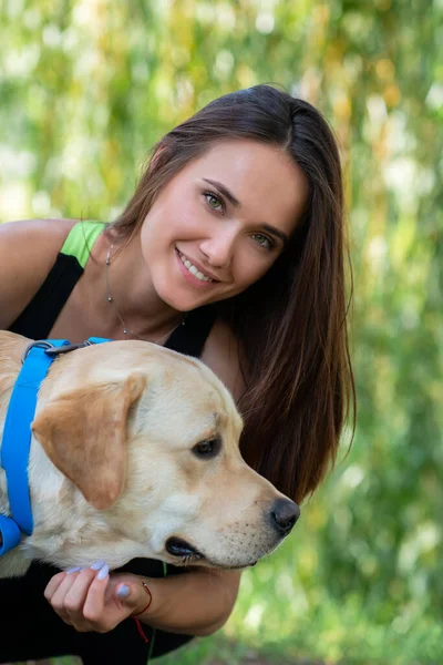陽気なかなり若いです女性座っていると抱擁彼女の犬で川の銀行で夏の公園 — ストック写真