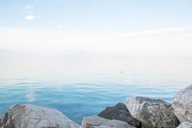 Desenzano del Garda, İtalya. İtalyan Gölü 'nün sakin manzarası Garda. Suyla, gökyüzüyle ve dağlarıyla sisli muhteşem bir manzara. Etrafı dağlarla çevrili muhteşem Garda Gölü manzarası. Yeryüzündeki cennet.