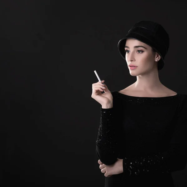 若いファッション女性は暗い背景の上に帽子と黒のドレスでタバコを吸っています ヴィンテージの女性の肖像画 スタイリング 画像トーン — ストック写真