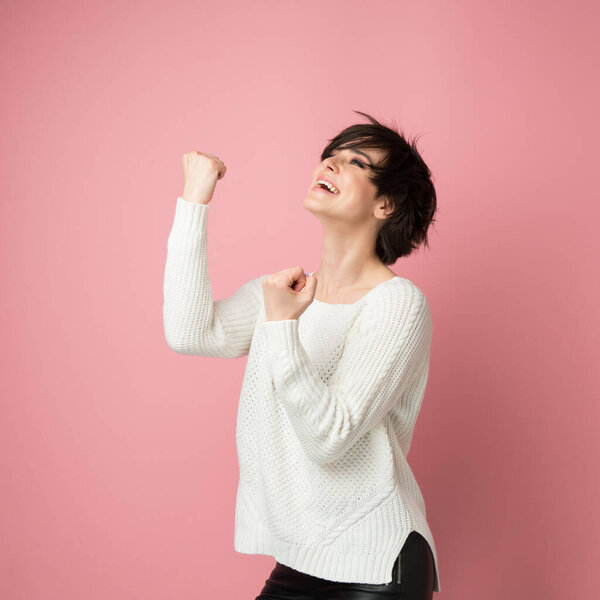 Beautiful young woman happy and excited expressing winning gesture. Successful and celebrating victory, triumphant, studio shot over pink background