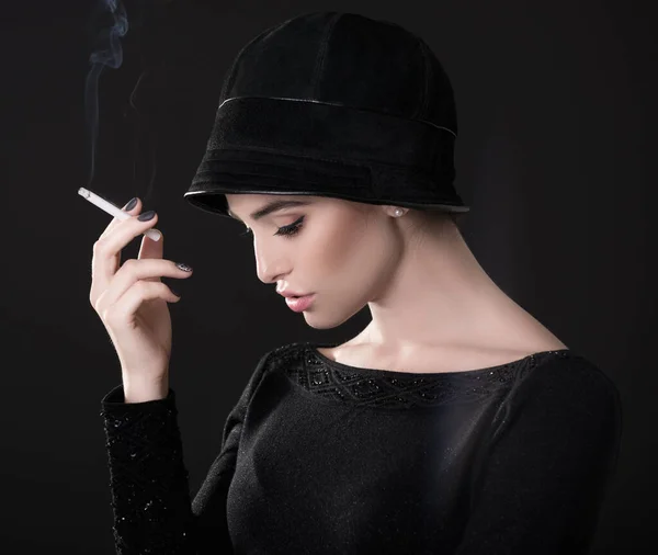 年轻的时尚女性戴着帽子抽烟 黑色的背景笼罩在黑暗之中 老式女性肖像 图像调色 — 图库照片