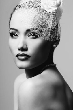 Beyaz şapkalı, duvağı ve gülleri olan güzel bir bayan, retro cazibeli güzellik portresi. Makyajlı güzel bir kadın kameraya bakıyor, şık bir görünümü var. Siyah beyaz inci küpeli kız.