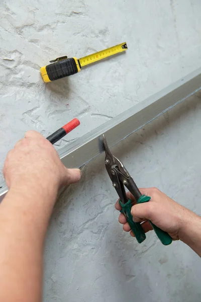 Male worker works with profile for drywall, cuts it with metal shears. Construction work, repair. Renovation