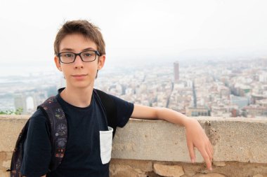 Alicante (İspanya) panoramasının arka planında poz veren gözlüklü yakışıklı genç bir çocuk. Santa Barbara Dağı 'ndan şehrin gençlik manzarası 