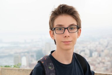 Alicante (İspanya) panoramasının arka planında poz veren gözlüklü yakışıklı genç bir çocuk. Santa Barbara Dağı 'ndan şehrin gençlik manzarası 