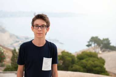 Alicante panoramasının üzerinden denize bakan gözlüklü yakışıklı bir genç. İspanya 'nın Akdeniz kıyısında gülümseyen güzel bir genç çocuk. Seyahat, yaz tatili, turizm, gençlik yaşam tarzı.