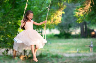 Happy girl rides on a swing in park. Little Princess has fun outdoor, summer nature outdoor. Childhood, child lifestyle, enjoyment, happiness. clipart