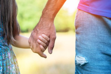 Erkek ve çocuğun elleri. Baba çocuğuna önderlik ediyor, yaz doğası. Ebeveynlik, birliktelik, yardım, birlik, çocukluk, güven, aile kavramı.