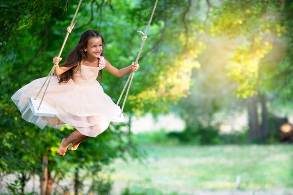幸せな女の子は公園でスイングに乗っています リトルプリンセスは楽しい屋外 夏の自然屋外があります 子供時代 子供のライフスタイル 楽しみ — ストック写真