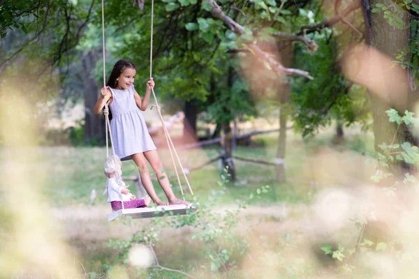 幸せな女の子は公園で彼女のレトロな人形とロープスイングに乗ります リトルプリンセスは楽しい屋外 夏の自然屋外があります 子供時代 子供のライフスタイル 楽しみ — ストック写真