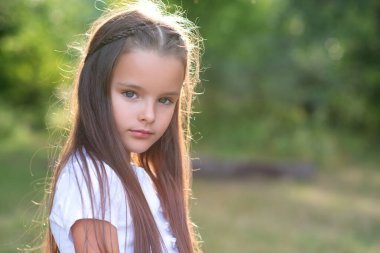 Uzun kahverengi saçlı, yaz havasında poz veren güzel bir kız. Çocuk portresi. Güzel çocuk yüzü