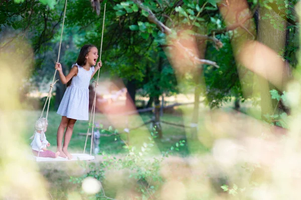 幸せな女の子は公園で彼女のレトロな人形とロープスイングに乗ります リトルプリンセスは楽しい屋外 夏の自然屋外があります 子供時代 子供のライフスタイル 楽しみ — ストック写真