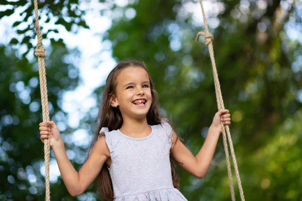 幸せな女の子は公園でスイングに乗っています リトルプリンセスは楽しい屋外 夏の自然屋外があります 子供時代 子供のライフスタイル 楽しみ — ストック写真