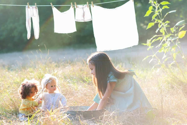 Little girl hangs out to dry retro doll clothes, summer nature outdoor. Washing, children\'s games, kid\'s leisure, vintage style.