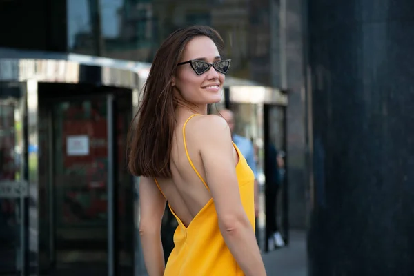 外でポーズをとるファッショナブルなかなりスタイリッシュな女の子 ストリートファッション 美しい若いブルネットの笑顔の女性は黄色のドレスと黒のサングラスを着て街の中心部を歩く 夏の屋外 — ストック写真