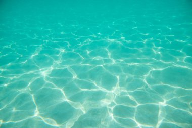 Suyun altında. Koltuğun altında güneş parıldıyor. Suyun altındaki dalgalar ve ışıldayan güneş ışınları. Derin turkuaz mavi deniz. Okyanus. Şeffaf su ve kumdaki ışık.