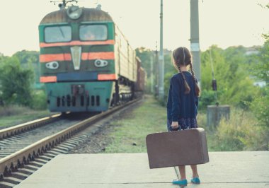 At kuyruklu güzel bir kız tren istasyonunda bekliyor. Koyu mavi elbiseli, çiçekli, bluzlu, elinde büyük bir bavul var. Genç gezgin, eski moda. Dışarıdaki şirin çocuk portresi.