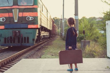 At kuyruklu güzel bir kız tren istasyonunda bekliyor. Koyu mavi elbiseli, çiçekli, bluzlu, elinde büyük bir bavul var. Genç gezgin, eski moda. Dışarıdaki şirin çocuk portresi.