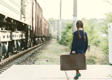 At kuyruklu güzel bir kız tren istasyonunda bekliyor. Koyu mavi elbiseli, çiçekli, bluzlu, elinde büyük bir bavul var. Genç gezgin, eski moda. Dışarıdaki şirin çocuk portresi.