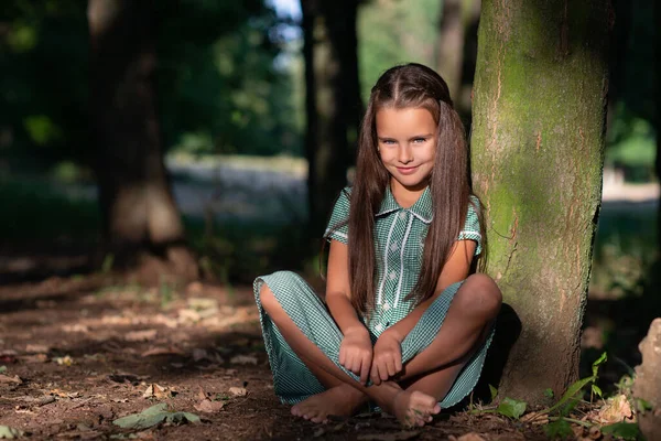 美しい顔で太陽の光と木の近くの森の中に座っているかなり小さなブルネットの女の子 子供の頃 かわいい子供屋外肖像画 — ストック写真