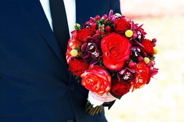 A vőlegény tartja világos lédús őszi esküvői csokor rózsák és az orchideák a vörös, bordó és sárga tónusok — Stock Fotó