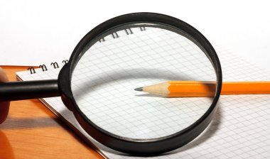 Büyüteç üstünde bir defter ve kalem