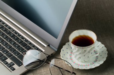 Dizüstü bilgisayar, gözlükleri ve bir fincan çay