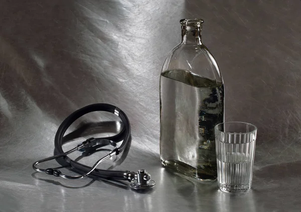 Botella de vodka, vidrio y estetoscopio sobre un fondo metálico — Foto de Stock
