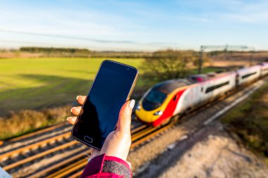Kadın el smartphone İngiltere'de demiryolu üzerinde tutarak gün görünümü.
