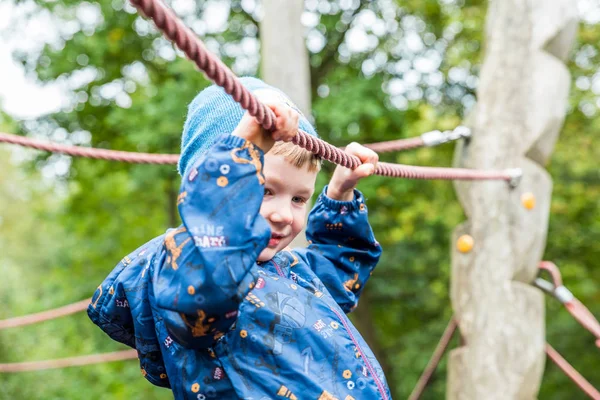 Blond chłopiec wspinaczka liny na jesień plac zabaw na świeżym powietrzu — Zdjęcie stockowe