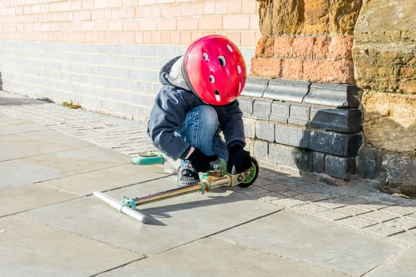Child boy red safety helmet fixing his scooter — Stock Photo, Image