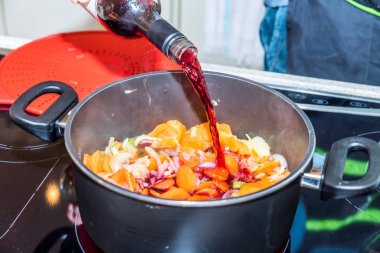 Erkek el holding şişe ve havuç ve soğan modern Elektrikli Ocak tarihinde kızartma ile pan güveç içine dökme kırmızı şarap