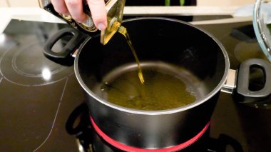 Erkek el tutan şişe ve modern Elektrikli Ocak üzerinde Pan güveç içine zeytinyağı dökme