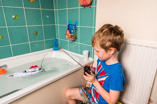 Blonde jongen met de Britse vlag op blauwe Tshirt spelen met radio controlled boot in badkamer — Stockfoto