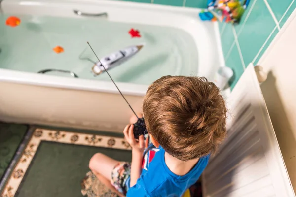 Garçon blond avec drapeau britannique sur Tshirt bleu jouant avec bateau radiocommandé dans la salle de bain — Photo