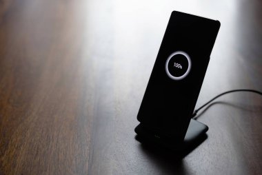 akıllı telefon kablosuz şarj standı üzerinde% 100 simge ahşap masada ekranda
