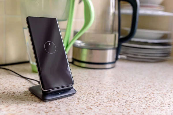 Smartphone carga inalámbrica en soporte de carga en la mesa de la cocina — Foto de Stock