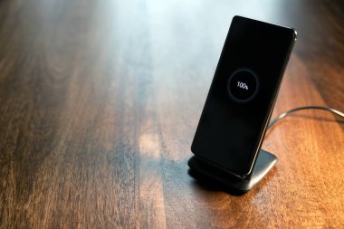 akıllı telefon kablosuz şarj standı üzerinde% 100 simge ahşap masada ekranda