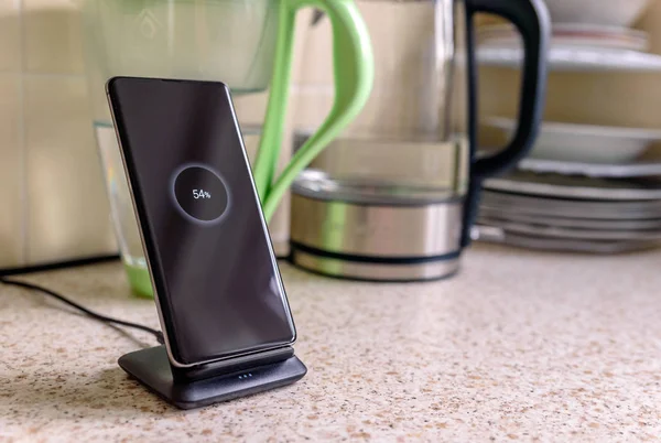 Carga inalámbrica smartphone en el soporte de carga con 54 por ciento icono en la pantalla en la mesa de la cocina — Foto de Stock
