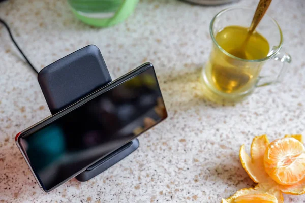 smartphone wireless charging on charging stand next to tea glass cup on kitchen tabletop