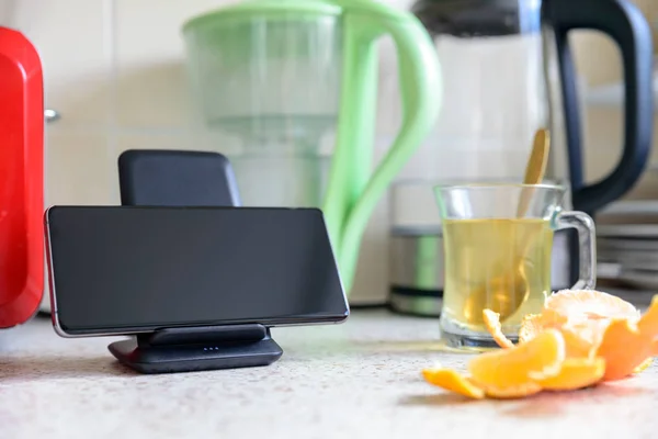 smartphone wireless charging on charging stand next to tea glass cup on kitchen tabletop