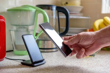 Akıllı telefon, mutfak masasının üstündeki şarj masasında şarj oluyor. Erkek el telefonu şarja yerleştiriyor