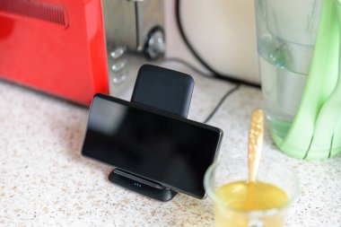 akıllı telefon kablosuz şarj oluyor mutfak masasında çay fincanının yanında duruyor