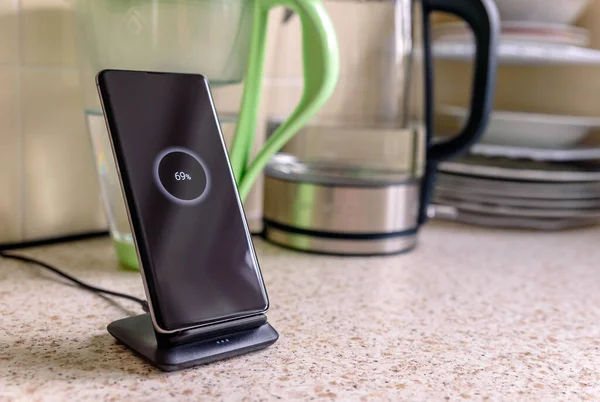 Carga inalámbrica smartphone en el soporte de carga con 69 por ciento icono en la pantalla en la mesa de la cocina — Foto de Stock