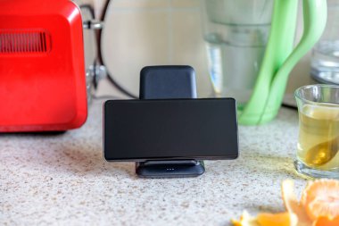 akıllı telefon kablosuz şarj oluyor mutfak masasında çay fincanının yanında duruyor