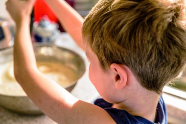 Çocuk mutfakta çırpıcıyla krep yapıyor.