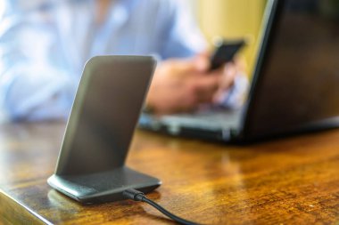 Kablosuz telefon şarjı. Ofiste elinde akıllı telefon olan bir adam var.